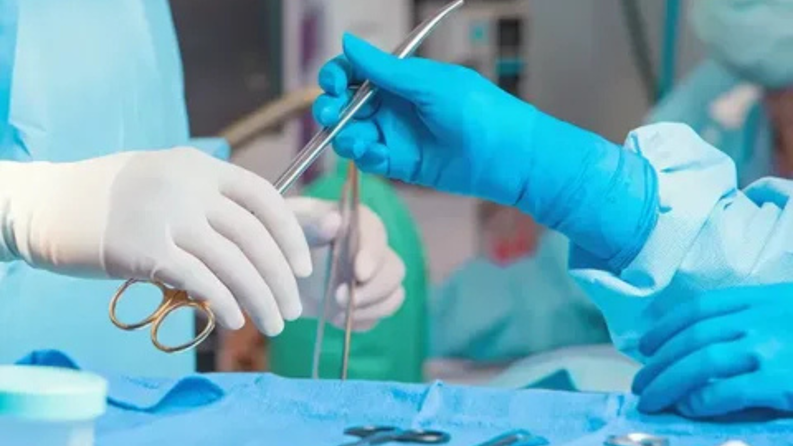 A close-up of two hands in surgical gloves exchanging medical instruments during an operation in an operating room.